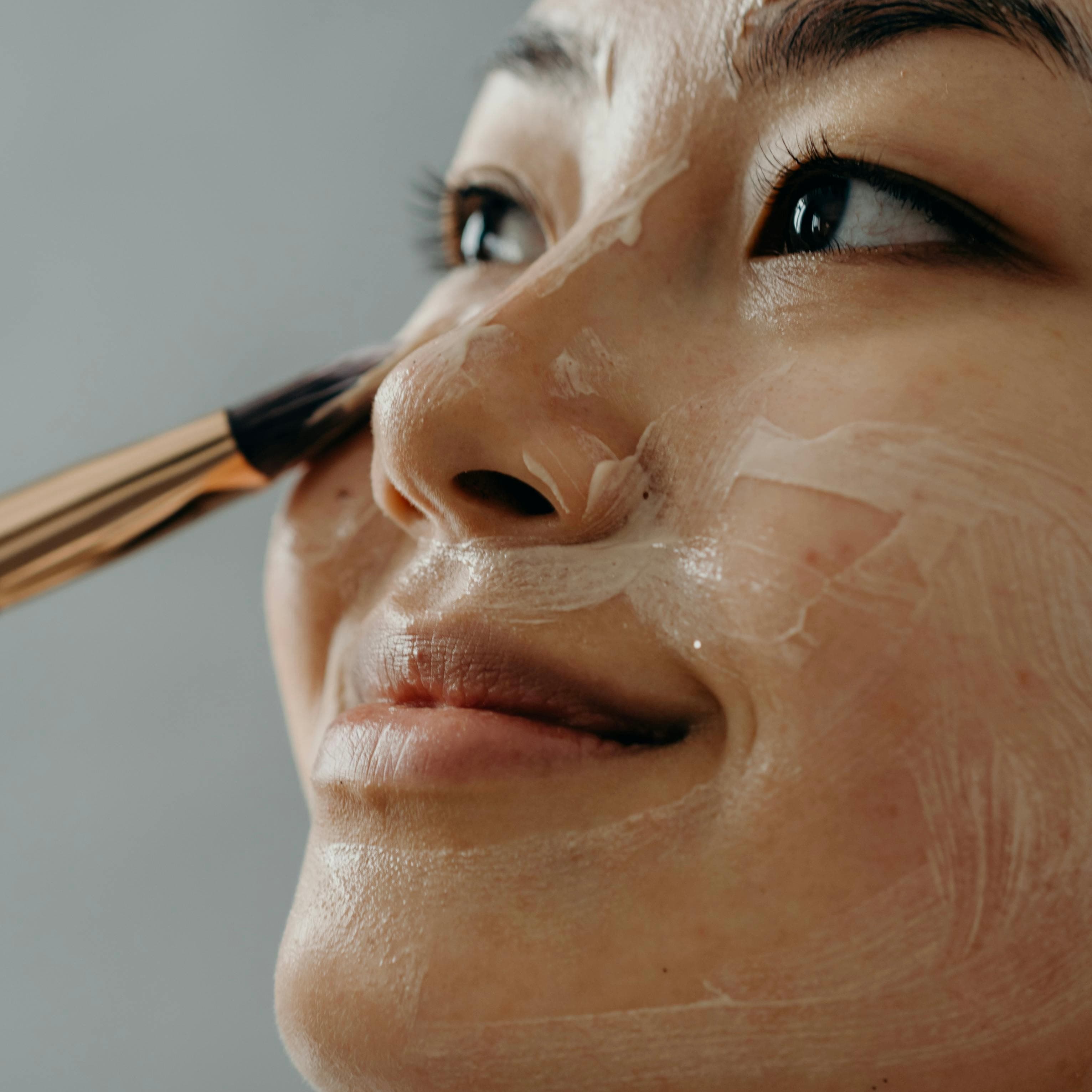 Close-up of a woman applying a facial mask with a brush, representing age-appropriate skincare treatments for glowing, healthy skin.